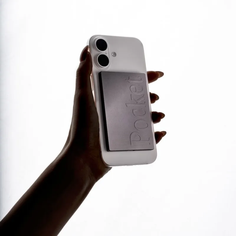 Pocket AI recorder, a thin metal card, attached to the back of a white iPhone held in a hand