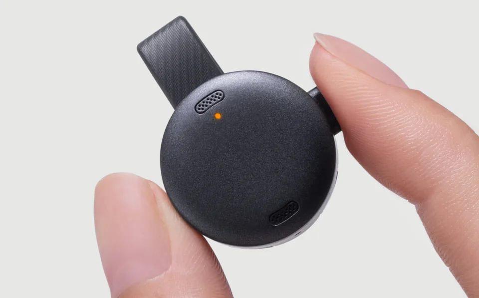 Soundcore Work coin sized recorder held between two fingers, black clip and orange status light